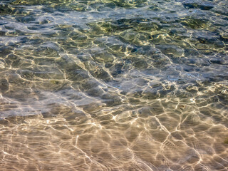 Texture of crystal clear light blue and turquoise transparent water with fine white sand base with bright reflection of sun in water movement. Water background