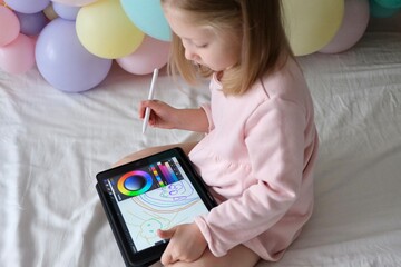 A little girl drawing a stylus on a tablet. A little girl uses a tablet. A drawing tablet. Child...