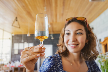 Happy asian woman tastes a new brand of cognac or grappa from a glass at the winery. The concept of strong alcohol and brandy - obrazy, fototapety, plakaty