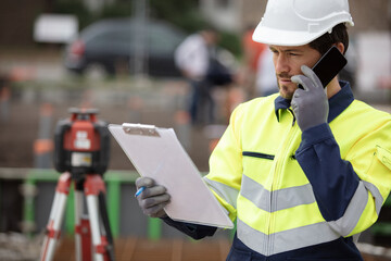 surveyor with clipboard on site using smartphone