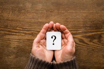 White card of question mark on mature woman palms on dark brown wooden table background. Point of view shot. Concept of what to do in old ages. Pensioner issues. Closeup. Top down view.