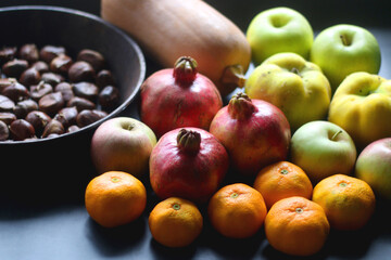 Pan with chestnuts, butternut squash and various fruit on dark background. Selective focus.