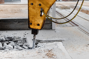 Professional demolition of reinforced concrete structures with an industrial hydraulic hammer with an excavator. Dismantling the concrete floor in the production area. Debris and crumbs of concrete.
