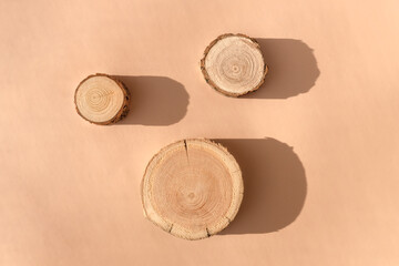 Three wooden disks lying on a trendy beige background. A platform made of trees for luxury and...