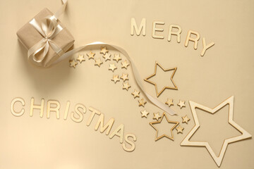 A gift wrapped in natural paper and a satin ribbon on a beige background decorated with wooden stars. Christmas inscription made of wooden letters.