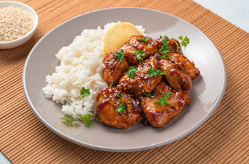 A portion of teriyaki chicken with rice and sesame seeds on a beige plate.