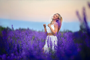 beautiful young girl in a white dress and a straw hat on a field of purple flowers