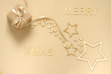 A gift wrapped in natural paper and a satin ribbon on a beige background decorated with wooden stars. Christmas inscription made of wooden letters.
