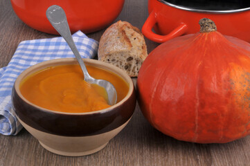 Bol de soupe de potimarron avec une cuillère avec ses ingrédients et du pain en gros plan