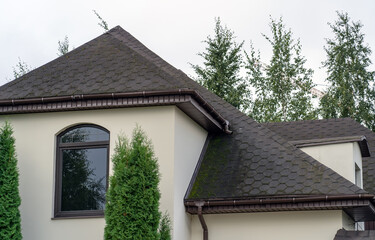 Corner of house with old roof from bituminous tile with moss and rain gutter. Metallic Guttering System, Guttering and Drainage Pipe Exterior