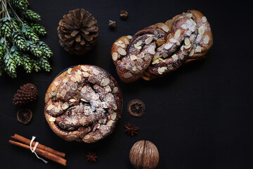 delicious homemade chocolate babka bread is on wooden black table with pinecone, anise stars and cinnamon sticks with black cement wall backgound of the bakery shop in the morining during Christmas