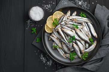 Sprat with lemon and salt on a black background.
