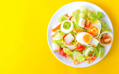 Delicious fresh vegetable salad on a white bowl on yellow background, top view.