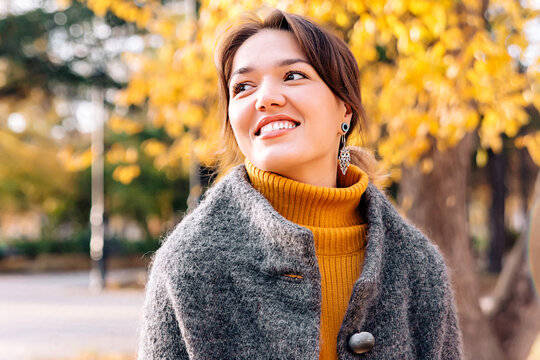 Portrait of a beautiful girl in an autumn park on the street dressed in a gray polto and yellow sweater dress. Smiles and looks away