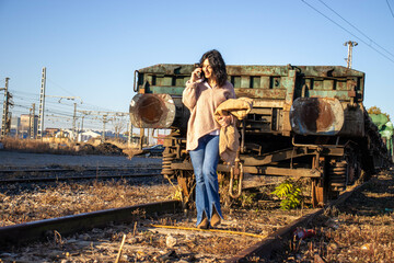 young brunette model on railroad tracks next to old freight train wreck walking with seasonal model