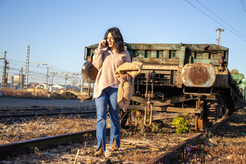 young brunette model on railroad tracks next to old freight train wreck walking with seasonal model