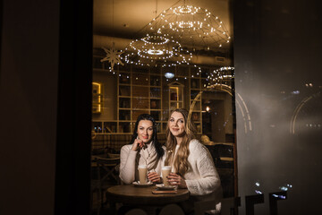 two beautiful young women in a cafe with coffee mugs by the window in winter