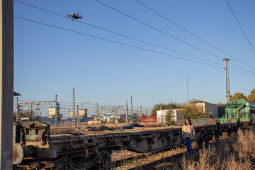 brunette and young model on railroad tracks next to scrapped old freight train and drone filming photo reportage