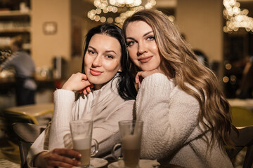 two beautiful women are sitting at a table in a cafe in a very cozy atmosphere in light warm clothes