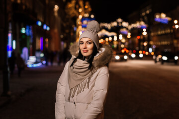 Fototapeta premium beautiful young woman in warm clothes against the background of blurry lights of the city in the background