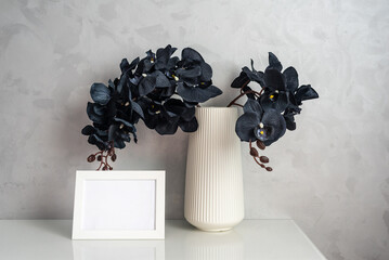 Unusual tropical orchid flowers with black petals in vase and photoframe with space for text on cabinet by light grey wall