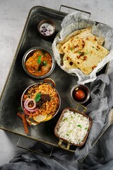 Indian meal thali - mutton biryani, raita, malai kofta, basmati rice, butter naan and gulab jamun served on a tray
