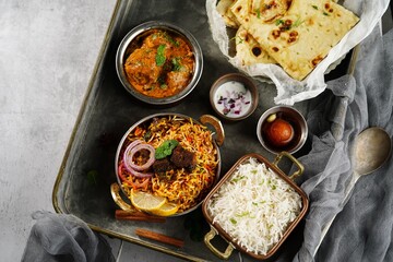 Indian meal thali - mutton biryani, raita, malai kofta, basmati rice, butter naan and gulab jamun served on a tray