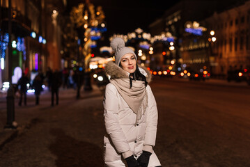 portrait of a beautiful young woman walking in the winter along the evening street in the lights. near the lights from the cars