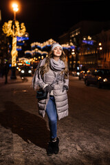 Fototapeta premium beautiful woman stands at night in the city glowing with lights in winter