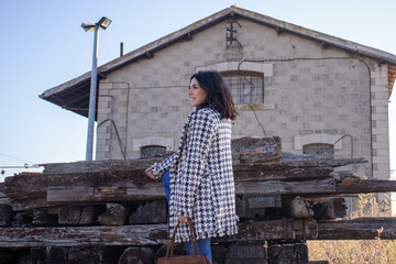 young dark-haired model with cheerful girl's cheerful face next to old industrial building, wearing checkered jacket