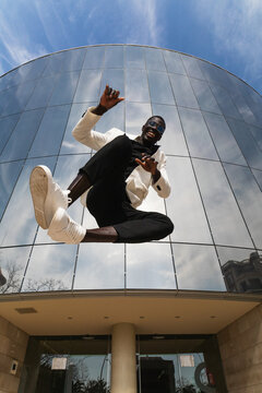 Happy black businessman jumping against modern urban building