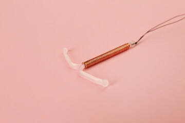 Copper intrauterine contraceptive device on light pink background
