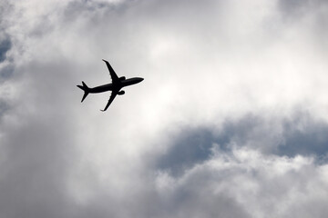 Fototapeta na wymiar Silhouette of airplane flying in sky with white clouds. Passenger plane at flight, travel concept