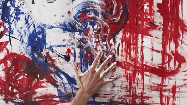 Impressionistic art school. Expressive female painter. Creative process. Unrecognizable woman painting red blue splashes and stamps with hands on white wall canvas.
