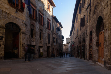 Fototapeta na wymiar Gasse in San Gimignano i schatten mit Fassaden und Personen bei blauem Himmel