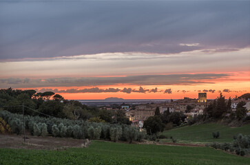 Mittelalterliche Stadt n der Dämmerung mit Olivenhain und Weinberg vor Mittelmeer, Wolken  bei Sonneuntzergang 