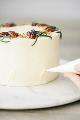  Confectioner finishing cake with pastry bag, close-up on hands. Wood and grey background.