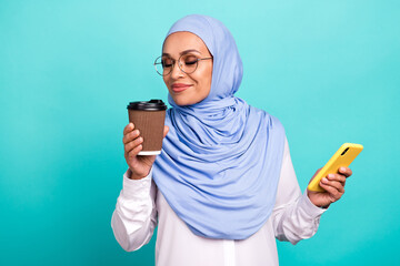 Photo of cute pretty young woman wear arab headscarf spectacles enjoying tea aroma modern gadget...