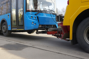 A tractor  is towing a faulty bus along a city street. Bus towing with partial loading.