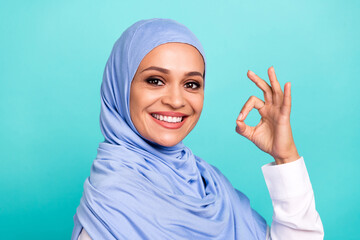 Photo of pretty adorable young lady dressed islamic hijab smiling showing okey sign isolated teal color background