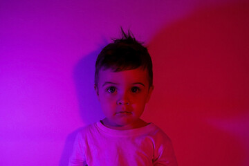Boy child portrait in a white T shirt in neon purple light on the background of the wall, toddler boy violet light 