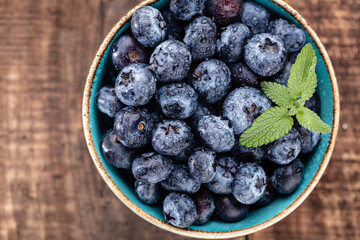 Ripe blueberries with water drops in a bowl on a wooden background,