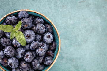 Ripe blueberries with water drops in a bowl on a pastel background,