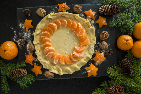 Christmas holiday cake making:  mandarines, fir branches, nuts on black slate top view