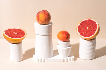 Fruits (grapefruit, peaches and apricots) in calming coral colors in white stands and podiums. Сonceptual creative still life, peachy pastel colors, hard shadows, pop-art style. Healthy food concept