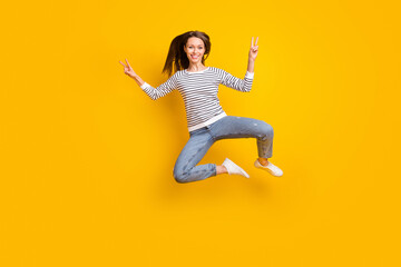 Fototapeta na wymiar Full size photo of lovely brunette millennial lady jump show v-sign wear sweater jeans sneakers isolated on yellow color background