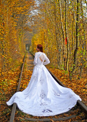 Pani młoda w sukni ślubnej z trenem na torach w tunelu z drzew