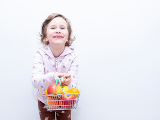 The child smiles and looks into the camera. Caucasian girl 6 years old, holding fresh fruits in her hands. ...