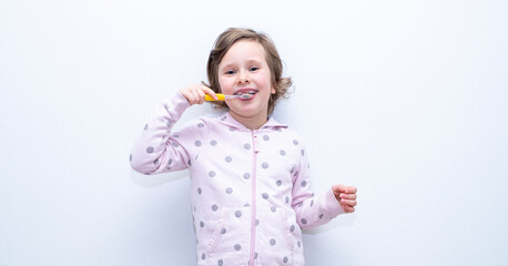 The child thoroughly brushes his teeth with a toothbrush and toothpaste. Hygiene of teeth and oral cavity. Caucasian girl on a gray background.