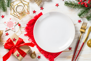 Christmas table with white plate and holiday decorations at white wooden table. Top view with copy space.